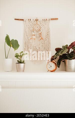 Camino in legno bianco con macrame e sogni catcher sulla parete, con piante casa e allarme rame vintage sulla mensola fuoco posto Foto Stock