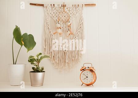 Camino in legno bianco con macrame e sogni catcher sulla parete, con piante casa e allarme rame vintage sulla mensola fuoco posto Foto Stock