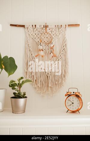 Camino in legno bianco con macrame e sogni catcher sulla parete, con piante casa e allarme rame vintage sulla mensola fuoco posto Foto Stock