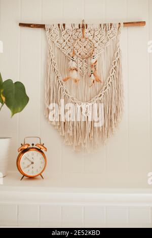 Camino in legno bianco con macrame e sogni catcher sulla parete, con piante casa e allarme rame vintage sulla mensola fuoco posto Foto Stock