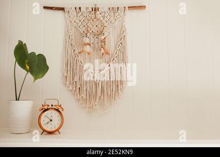 Camino in legno bianco con macrame e sogni catcher sulla parete, con piante casa e allarme rame vintage sulla mensola fuoco posto Foto Stock