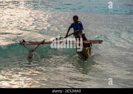 Giovani surfs locali una canoa Outrigger sulla spiaggia di Bougainville, Papua Nuova Guinea Foto Stock