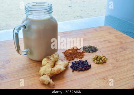 Bevanda calda fatta in casa Chai latte, con tutte le spezie utilizzate incluse, su un tagliere di legno. Foto Stock
