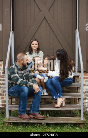 Una famiglia di cinque persone con due ragazze e un ragazzo bay seduto sui gradini in una zona urbana del centro. Foto Stock