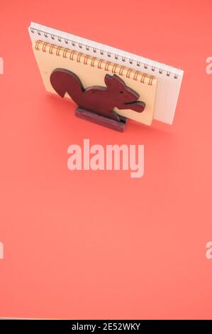 Scatto isolato verticale dei taccuini nello scoiattolo di legno supporto carta su sfondo rosa Foto Stock