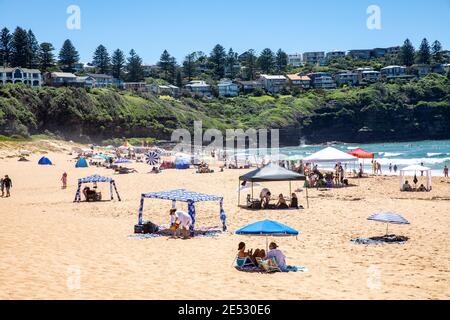 Prendi il sole sulla spiaggia di Bilgola Sydney durante la calda estate australiana e utilizza cabine e ombrelloni per fornire protezione solare e ombra, Sydney, New South Wales Foto Stock