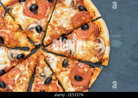 La pizza vegetariana fatta in casa con pomodoro e funghi tagliata a fette uno sfondo di ardesia Foto Stock