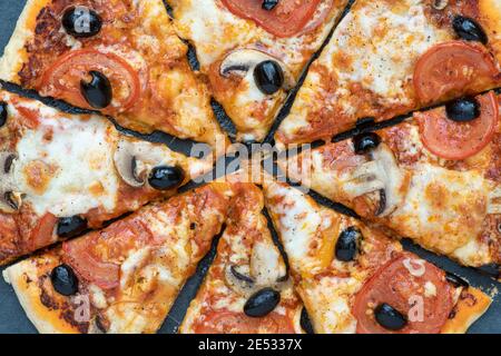 La pizza vegetariana fatta in casa con pomodoro e funghi tagliata a fette uno sfondo di ardesia Foto Stock