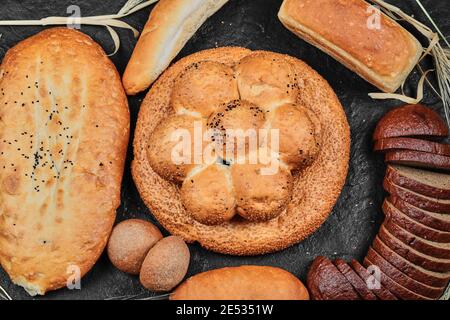 Fette di pane nero, focaccine, bagel e bastone su scrivania scura Foto Stock