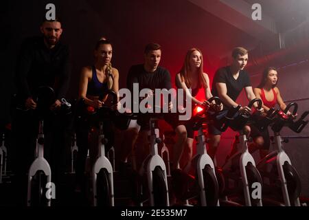giovani in bicicletta in classe di spinning in palestra moderna, allenandosi su cyclette. forte allenamento maschile e femminile su cyclette Foto Stock
