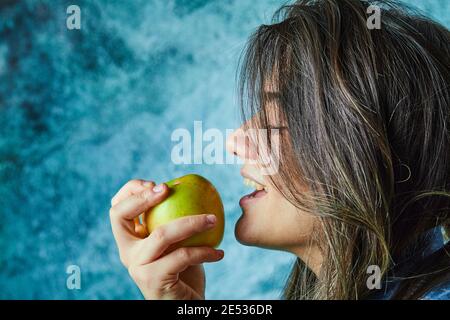 Donna che mangia mela su sfondo blu Foto Stock