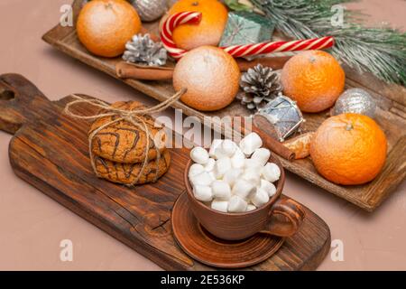 Caffè o cacao con marshmallows su una lunga tavola vintage in una composizione di Natale. Biscotti e tangerini con dolci al tavolo delle feste. Foto Stock