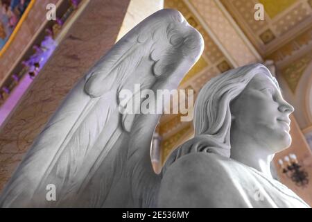 Primo piano di una statua in marmo bianco di un'alata angelo contro la navata di una chiesa colorata Foto Stock