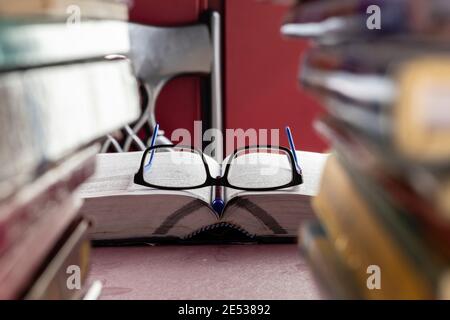 fuoco selettivo sugli occhiali su un libro aperto su un tabella di studio completa la pila di libri Foto Stock