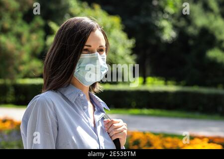 Bel ritratto di giovane donna in un parco estivo con una maschera medica protettiva. Foto Stock