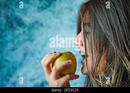 Donna che mangia mela su sfondo blu Foto Stock