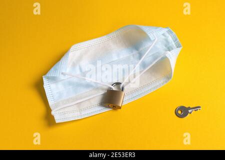 Blocco del mondo pandemico. Mondo chiuso per quarantena coronavirus. Maschera medica chiusa con serratura e chiave su sfondo giallo Foto Stock