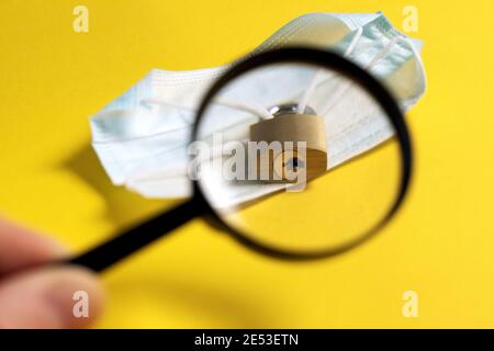 Cerca la possibilità di rimuovere il blocco. Fine del mondo isolamento di pandemia coronavirus. Maschera medica chiusa con serratura, buco di chiave attraverso la lente d'ingrandimento g Foto Stock