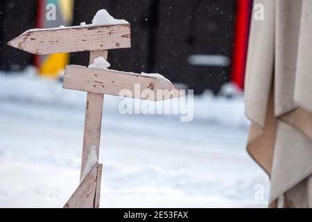 cartello in legno innevato con due frecce nlank su un colorato sfondo sfocato Foto Stock