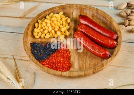 Salsicce, semi di mais bolliti e caviale su un piatto di legno Foto Stock
