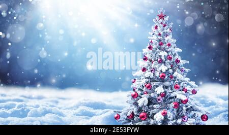 Albero di Natale innevato con palle rosse in un paesaggio invernale Foto Stock