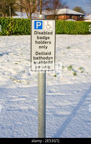 Un cartello indica un posto di parcheggio per i titolari di badge disabili solo in un parcheggio coperto di neve Foto Stock