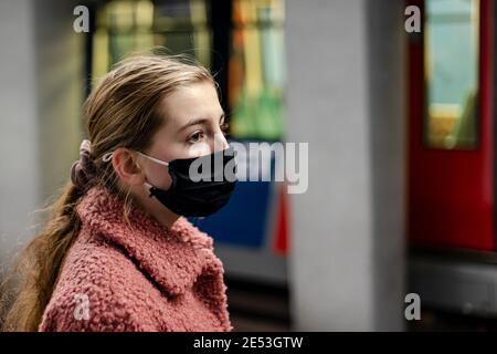 Ragazza che indossa una maschera che aspetta la metropolitana di Rotterdam. Stazione della metropolitana con un treno sullo sfondo. Foto Stock