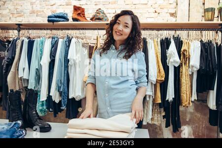 Donna shopping in una boutique. Donna che guarda la macchina fotografica e sorride durante lo shopping in un negozio di abbigliamento. Foto Stock