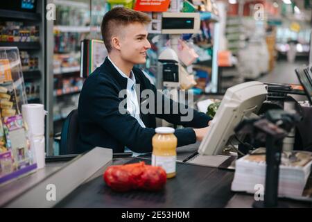 Uomo che lavora al negozio di alimentari checkout. Giovane lavoratore in vacanza lavoro al supermercato. Foto Stock