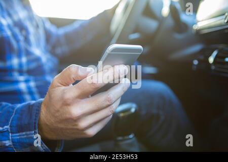 Primo piano di Man in Auto Texting su cellulare Durante la guida Foto Stock