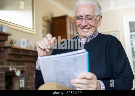 Sorridente uomo senior facendo Sudoku Puzzle a casa Foto Stock