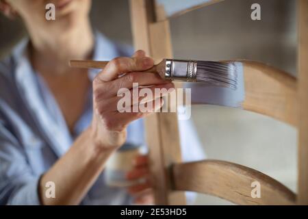 Primo piano di Donna Upcycling Mobili in officina a casa Pittura sedia di legno Foto Stock