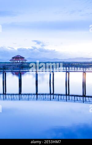 Un tranquillo lago tropicale e una passerella in legno la mattina d'estate, pittoresca passerella in legno con gazebo si riflette sul lago. Sam Roi Yod, Thailandia. Foto Stock