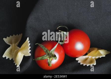 Vista dall'alto dei pomodori a base di spaghetti e farfale e delle spose con spezie sullo sfondo nero, Foto Stock