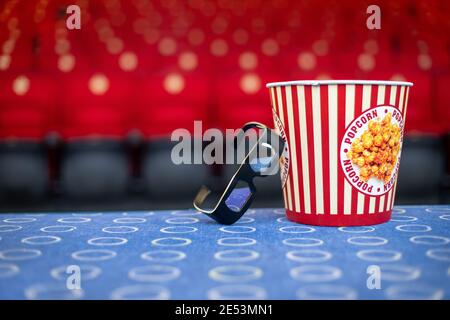 Un grande secchio di popcorn e occhiali 3D sul sfondo di sedie da cinema Foto Stock