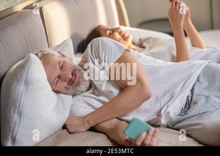 Uomo e donna con smartphone a letto Foto Stock