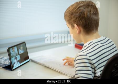 Adolescente ragazzo di scuola che ha lezione virtuale a casa usando il tablet durante il homeschooling alla quarantena pandemica Foto Stock