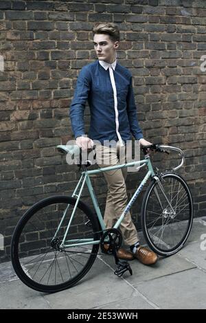 Bell'uomo caucasico in outfit alla moda in posa con una bicicletta d'epoca alla moda sulla strada di Shoreditch , Londra. Foto Stock