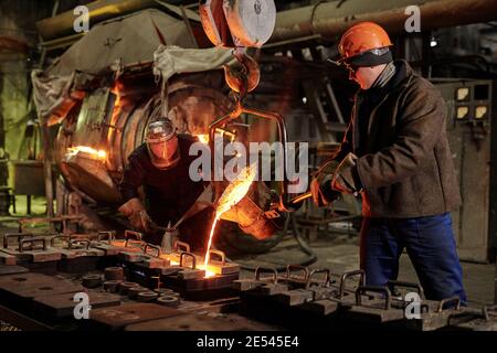 I lavoratori in caschi che lavorano in squadra si fondono il ferro dentro fabbrica di metallo Foto Stock