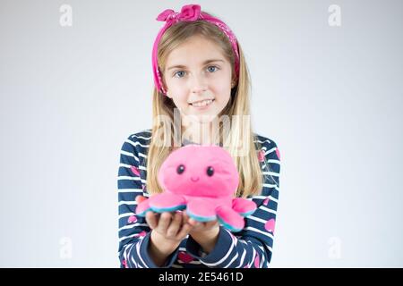 Bambina caucasica con capelli lunghi che indossa camicia a righe e che tiene il polpo giocattolo sorridente felice. Foto Stock