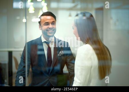 I millennial diversi in partner aziendali di outfit formali parlano dopo una riunione seduti in un moderno e luminoso luogo di lavoro. Bell'uomo d'affari giovane e. Foto Stock