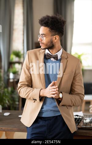 Giovane designer di moda che guarda lontano con vista penosa mentre si è in piedi vicino al suo posto di lavoro Foto Stock