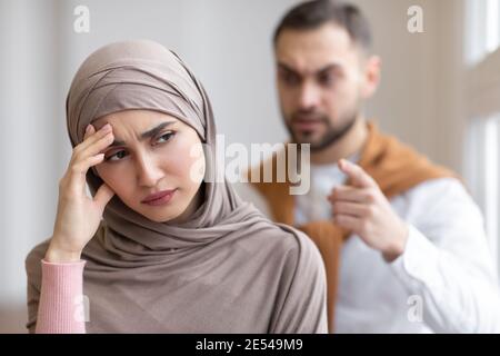 Marito musulmano aggressivo gridando alla moglie depressa in piedi a casa Foto Stock