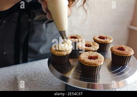 la ragazza cuoce cupcakes a casa. Mani di uno chef con un sacchetto di pasticceria, spremendo la crema sulle cupcakes Foto Stock