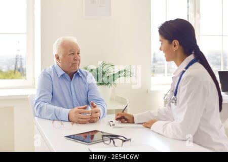 Anziano uomo paziente seduto e parlando con giovane donna medico durante la visita Foto Stock