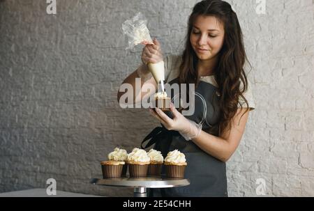 la ragazza cuoce cupcakes a casa. Mani di uno chef con un sacchetto di pasticceria, spremendo la crema sulle cupcakes Foto Stock
