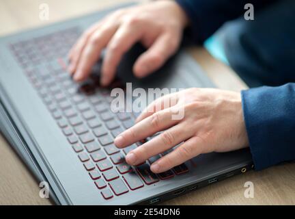 Le mani dell'uomo che digitano sulla tastiera di un computer portatile. Un uomo in ufficio scrive su un computer portatile. Messa a fuoco selettiva Foto Stock