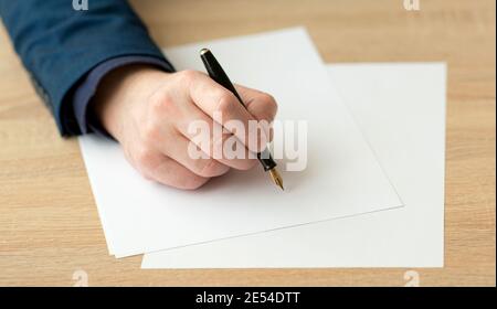 Closeup di mano di un uomo d'affari in un vestito, scrivendo una lettera o firma un documento su un pezzo di carta bianca con una penna stilografica con pennino Foto Stock