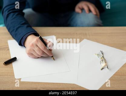 Uomo d'affari in ufficio scrive una lettera o firma una documento su un pezzo di carta bianca con una fontana penna con pennino Foto Stock