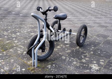 Un triciclo per bambini fissato con un lucchetto ad una bicicletta stare in piedi su un marciapiede Foto Stock